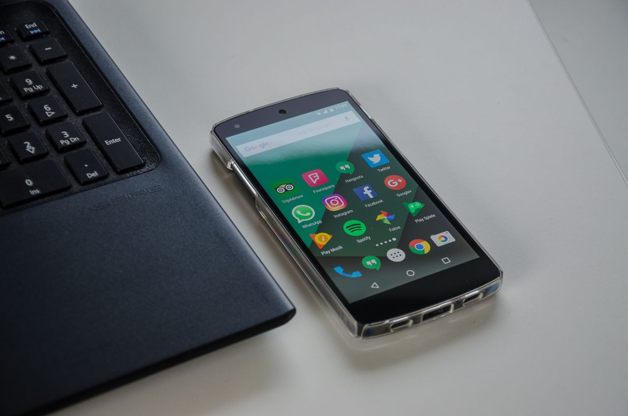 Smartphone on a table showing various social media apps beside a laptop keyboard.